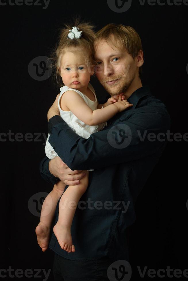 un padre tiene in braccio la sua piccola figlia di un anno. girato su sfondo nero. foto