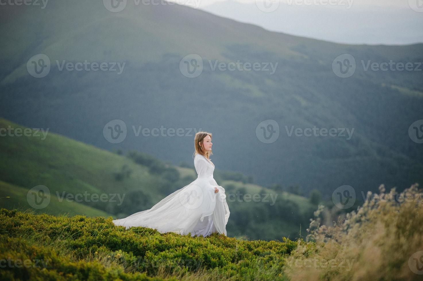 donna in abito da sposa corre attraverso il campo verso le montagne foto