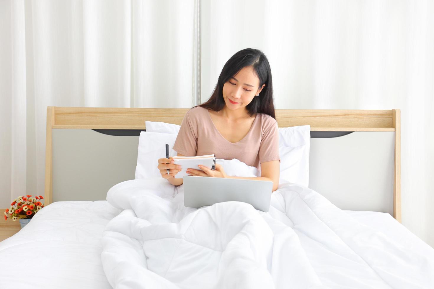 donna asiatica che lavora online da casa con il laptop sul letto per una nuova vita normale durante il periodo di quarantena da covid-19 foto