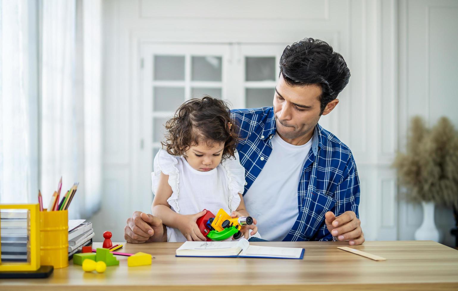 concetto di famiglia, paternità e infanzia - padre felice e figlia piccola che giocano con il microscopio giocattolo a tavola a casa foto