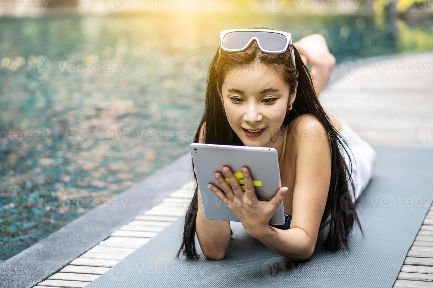 bella donna asiatica che si rilassa con l'utilizzo di un computer tablet digitale all'aperto a bordo piscina foto