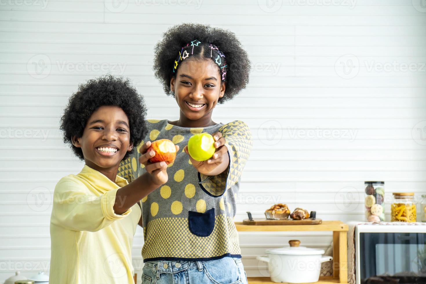 due bambini afroamericani si divertono e mostrano felice che la mela rossa e verde è morsa, goditi il momento di mangiare. cibo sano e concetto di bambino. foto