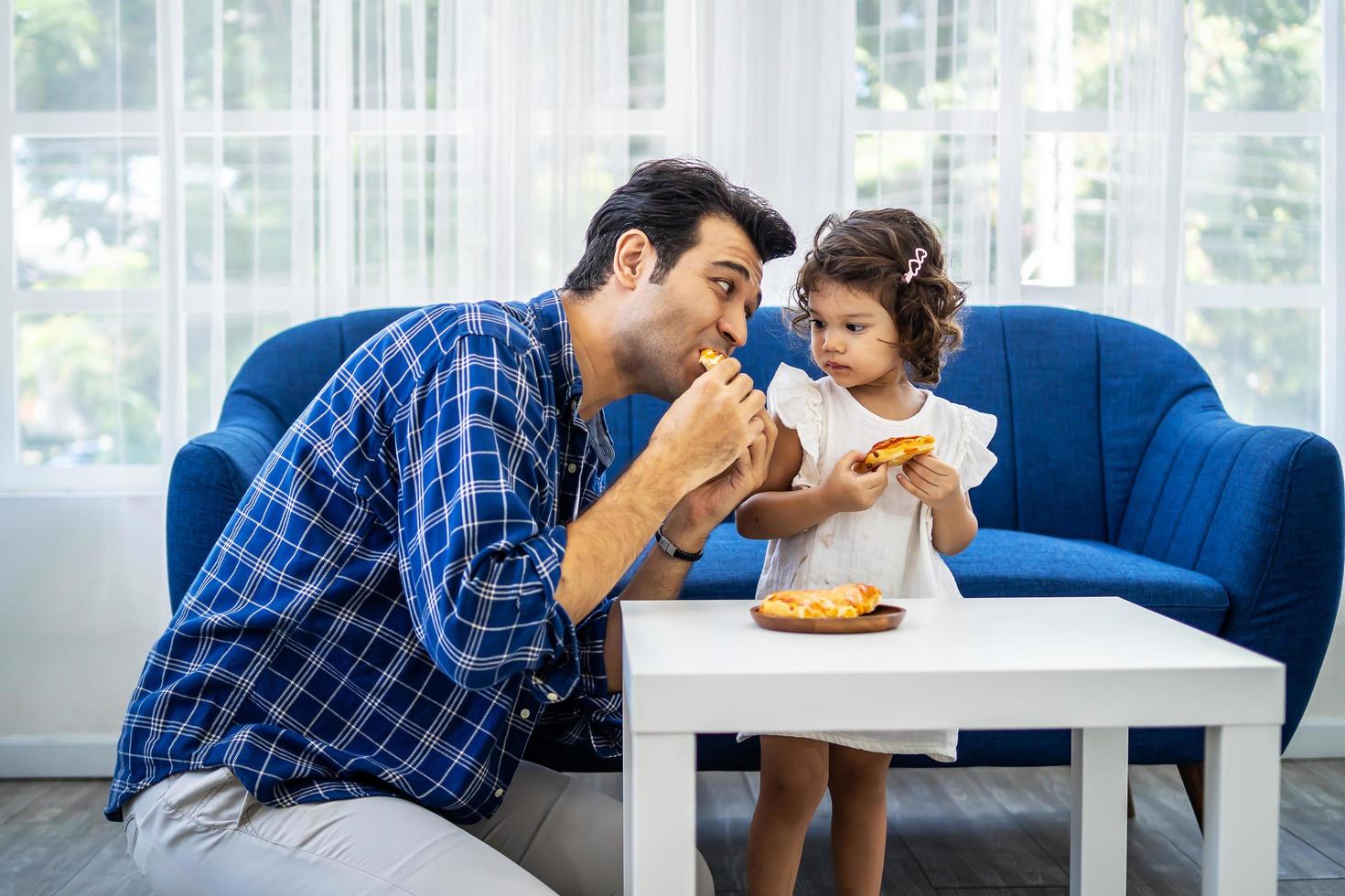 giovane padre attraente e piccola figlia carina che si godono la pizza nel comodo divano del soggiorno foto