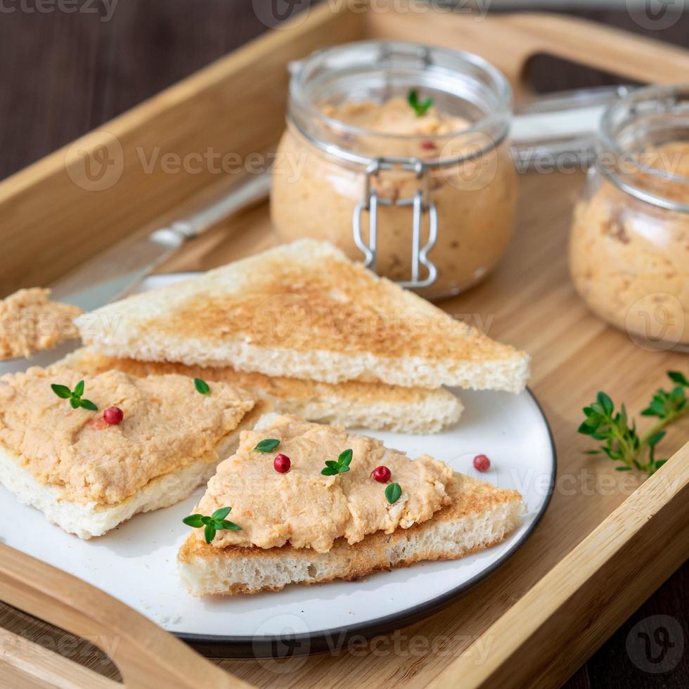 Patè di pollo fresco fatto in casa su pane tostato su vassoio su sfondo rustico, vista laterale foto