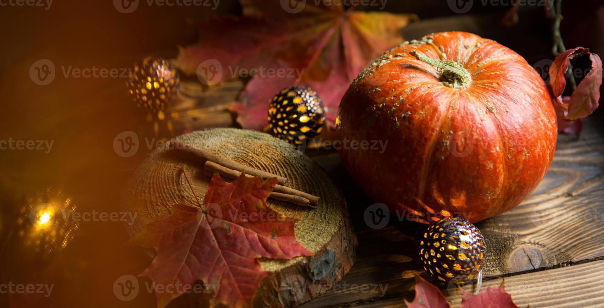 zucca rotonda naturale arancione su un tavolo di legno con foglie d'acero gialle e rosse cadute, bastoncini di cannella. ghirlande di luci, calda atmosfera autunnale, ringraziamento, festa del raccolto, halloween. copia spazio foto