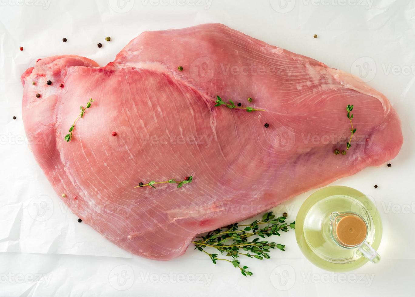 filetto di tacchino crudo con timo, pepe e olio d'oliva su carta pergamena bianca, vista dall'alto foto