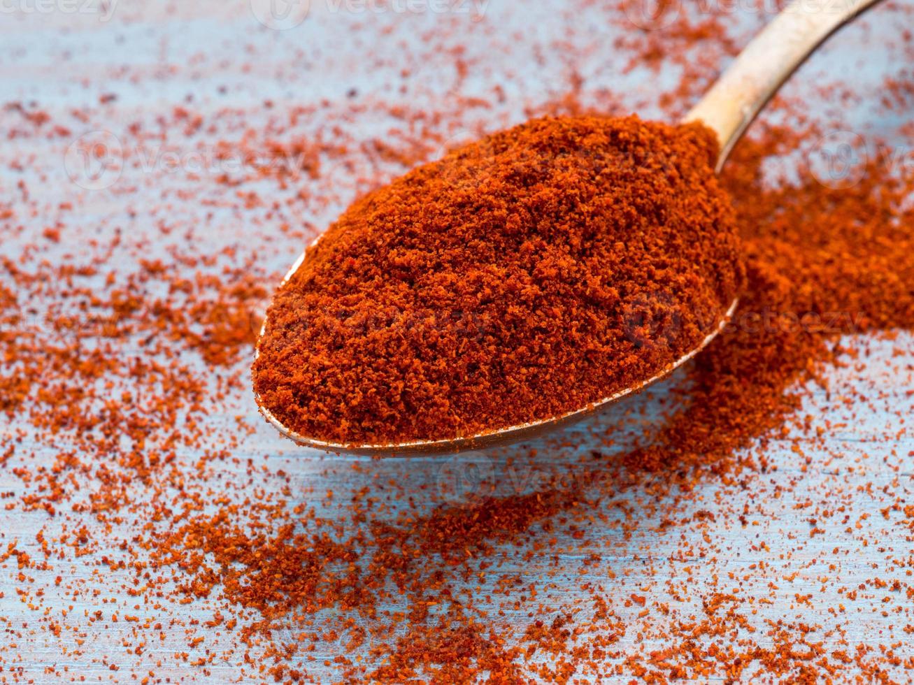 un cucchiaio colmo di spezie di paprika, polvere sparsa sul tavolo di legno blu brillante colore chiaro, primo piano, vista laterale foto