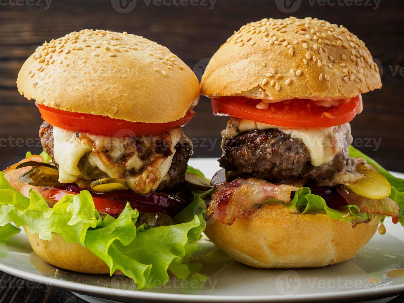 due deliziosi hamburger fatti in casa con cotoletta di manzo, formaggio, cipolla, pomodoro e lattuga su involtini tostati. fast food americano, alimentazione malsana. vista laterale. foto