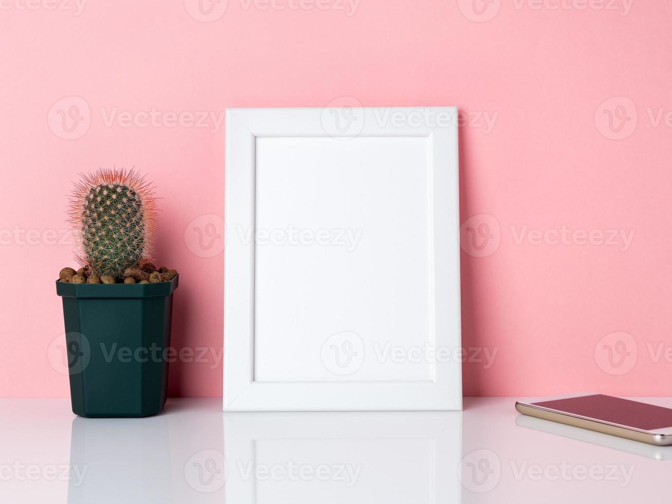 cornice bianca vuota e pianta di cactus su un tavolo bianco contro il muro rosa con spazio per la copia. mockup con spazio di copia. foto