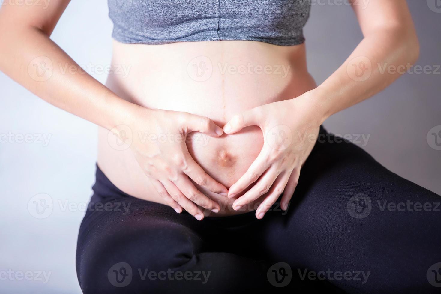 ritratto in sezione centrale di una donna irriconoscibile durante gli ultimi mesi di gravidanza che tiene delicatamente la sua grande pancia foto