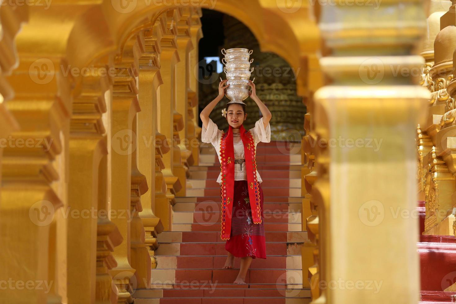 giovane ragazza asiatica in costume tradizionale birmano che tiene una ciotola di riso a portata di mano alla pagoda dorata nel tempio del myanmar. donne del Myanmar che tengono fiori con abiti tradizionali birmani che visitano un tempio buddista foto