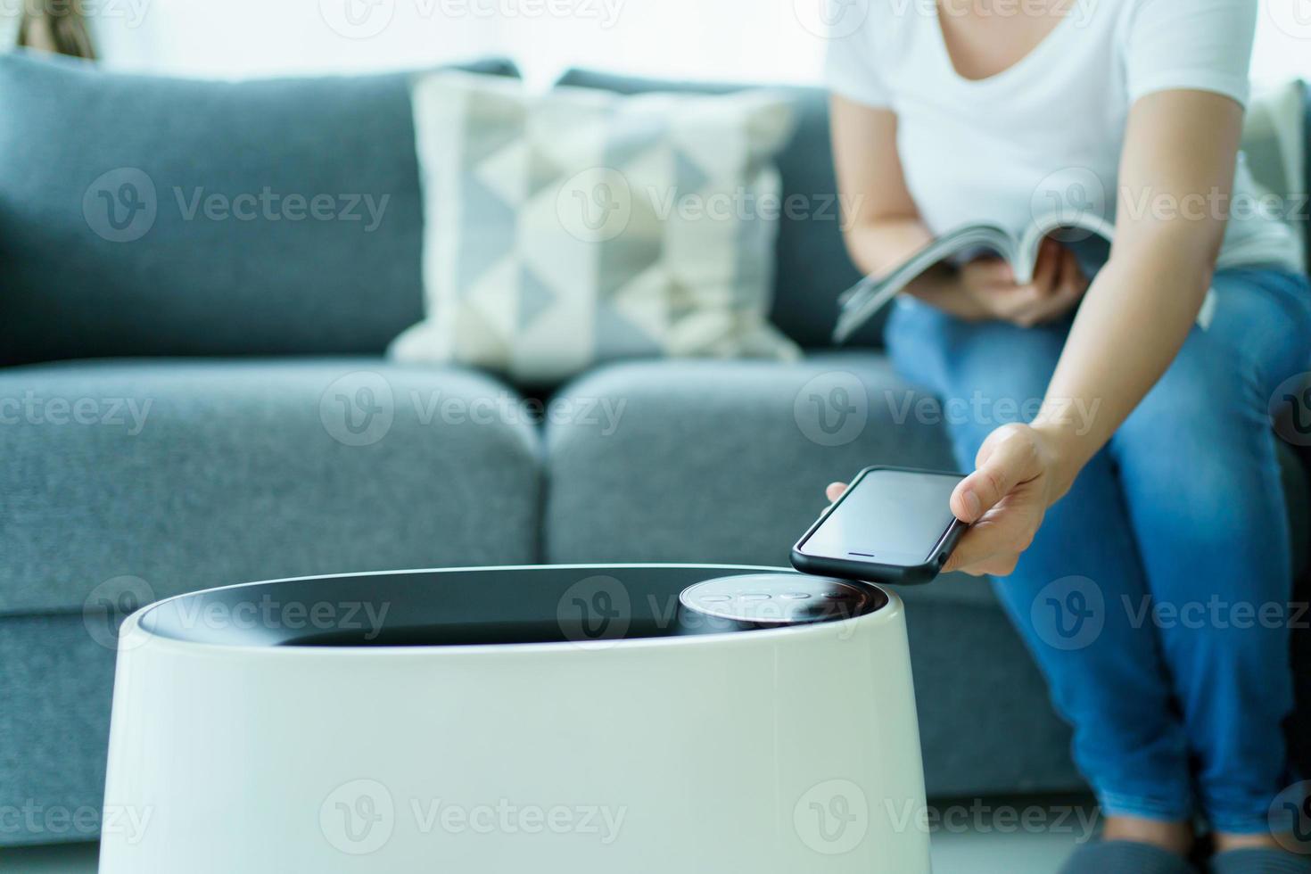la donna controlla un moderno purificatore d'aria attraverso l'applicazione su uno smartphone, uno schermo dello smartphone isolato di colore bianco. concetto di tecnologia di connettività domestica moderna e intelligente. foto