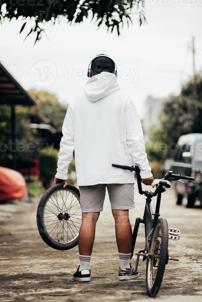 mockup con cappuccio con vista posteriore di un uomo in piedi con la sua bici foto