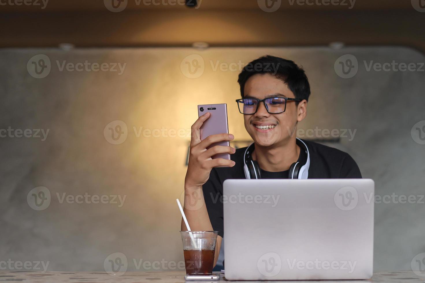 studente di college maschio asiatico intelligente che sorride e guarda al telefono per studiare online presso la caffetteria foto