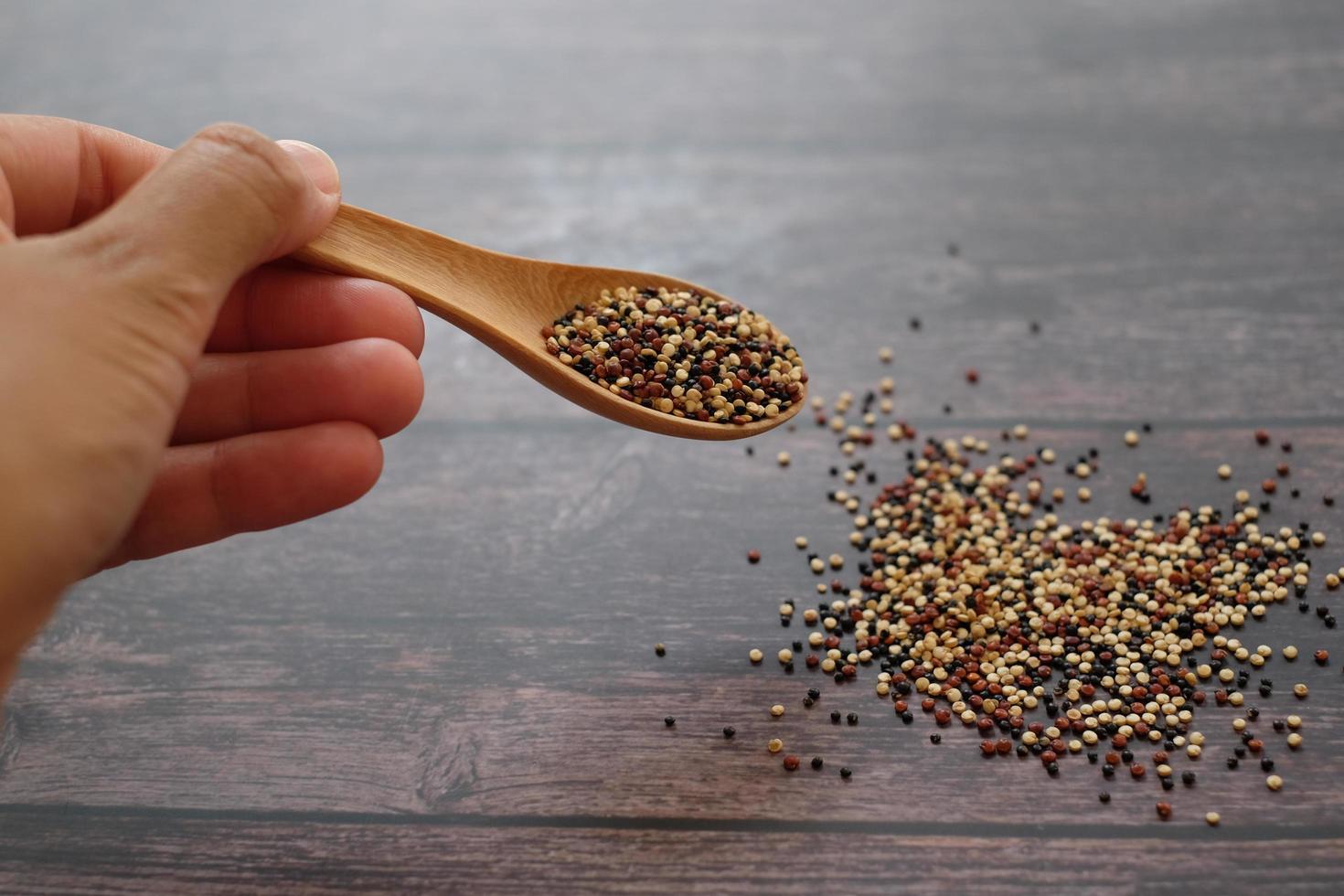 mano ravvicinata che tiene il cucchiaio di legno con semi di quinoa su sfondo tavolo in legno. la quinoa è una buona fonte di proteine per le persone che seguono una dieta a base vegetale. foto