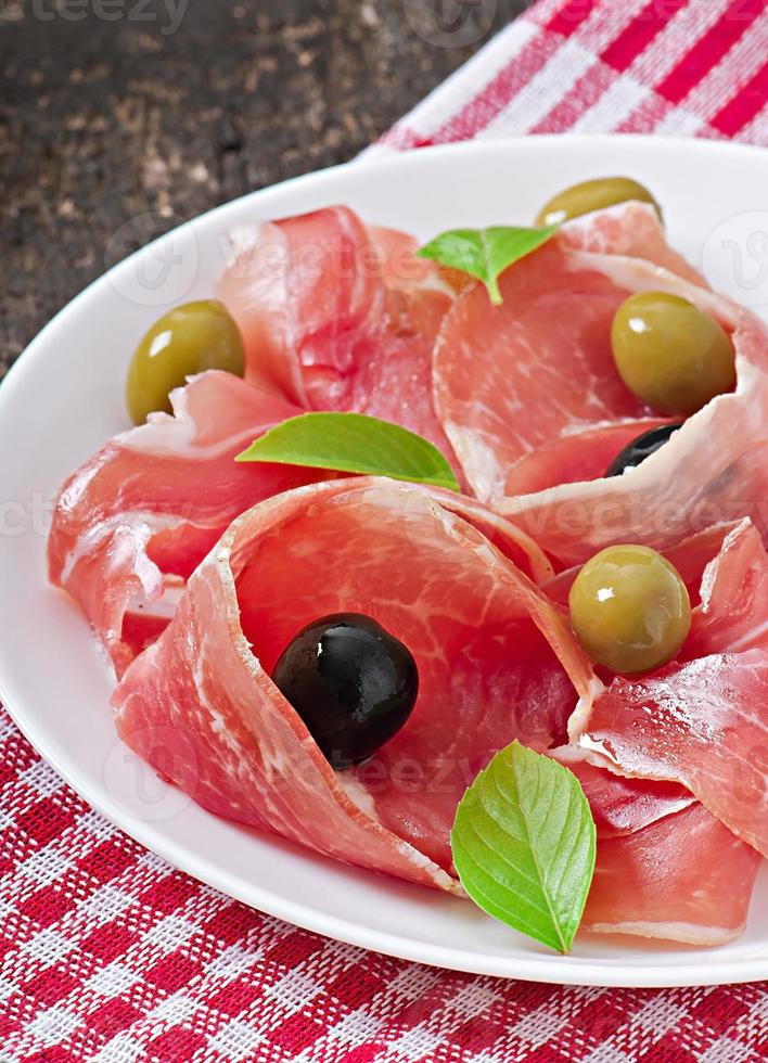 prosciutto, olive, basilico su fondo di legno vecchio foto