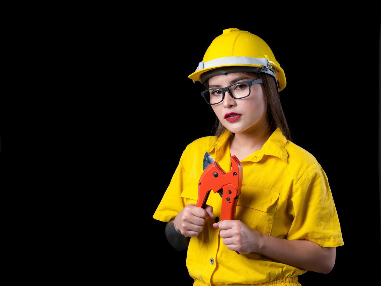 una bella donna nell'uniforme gialla del tecnico che tiene uno strumento di costruzione foto