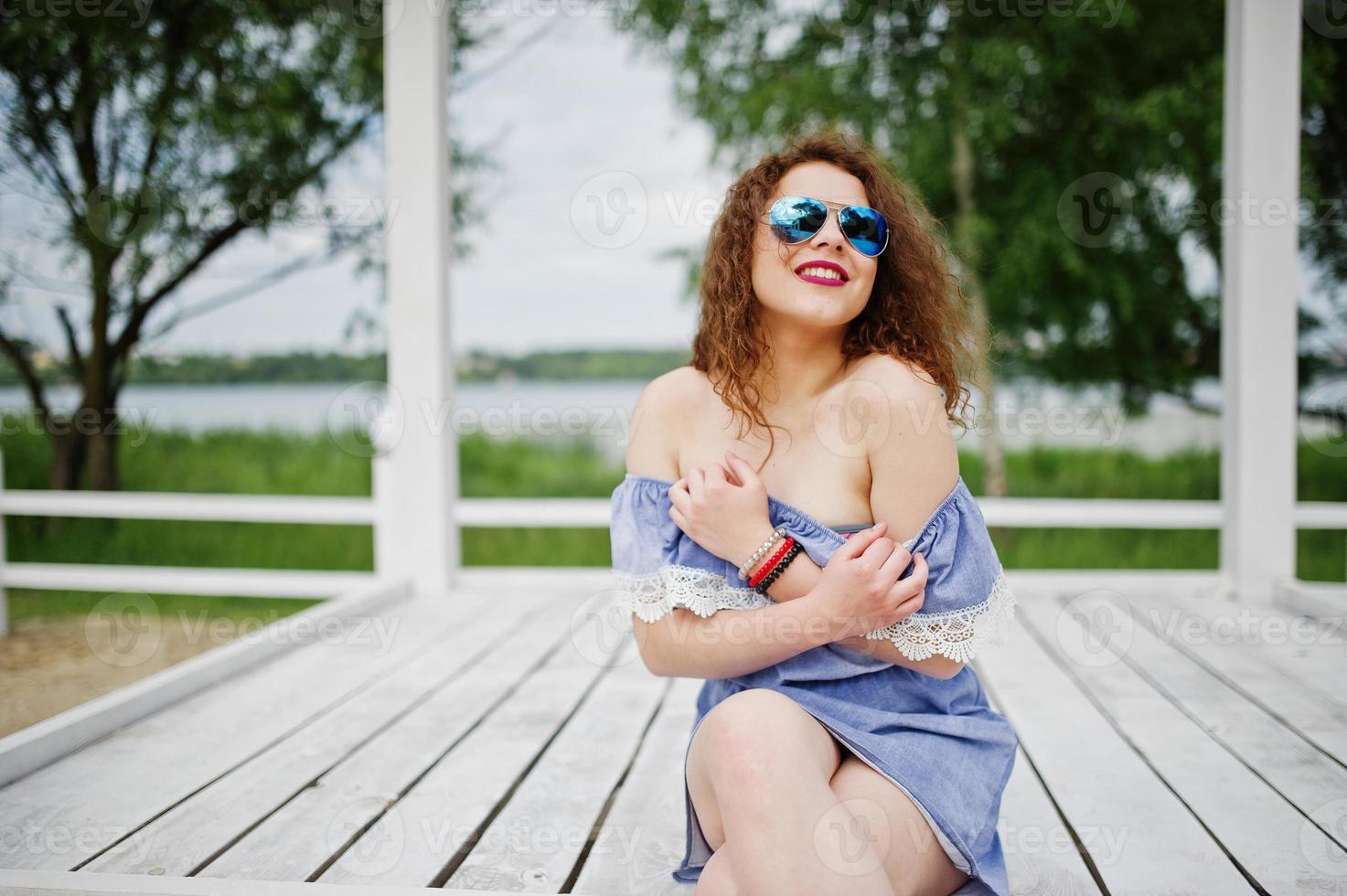 ritratto di una favolosa ragazza che indossa un abito chic in posa su una terrazza in legno bianco. foto