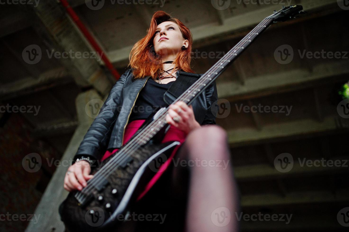ragazza punk dai capelli rossi indossa su gonna nera e rossa, con basso in un luogo abbandonato. ritratto di musicista donna gotica. foto