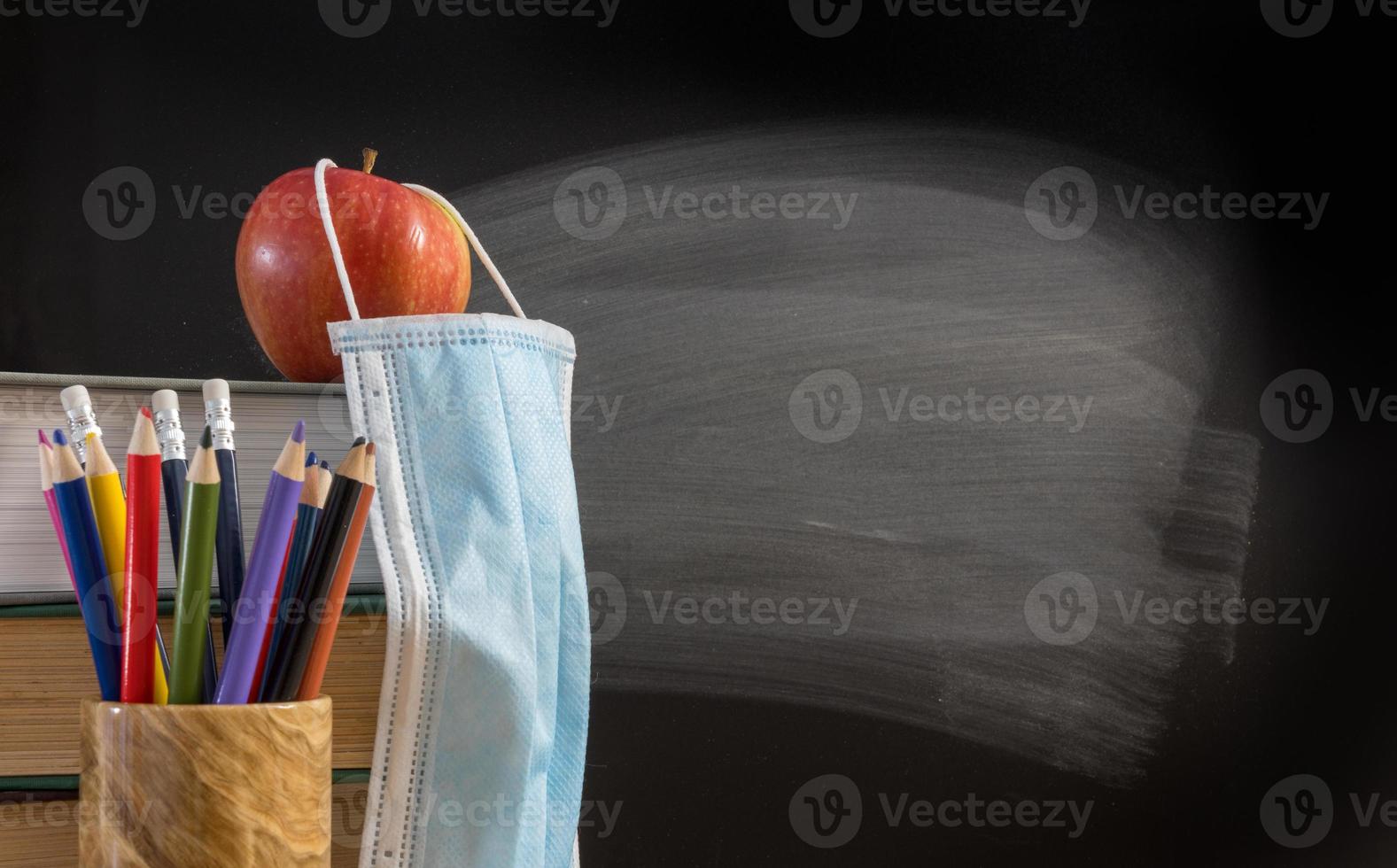 torna al concetto di sfondo della scuola virtuale con una pila di libri, matita, mela con maschera facciale foto