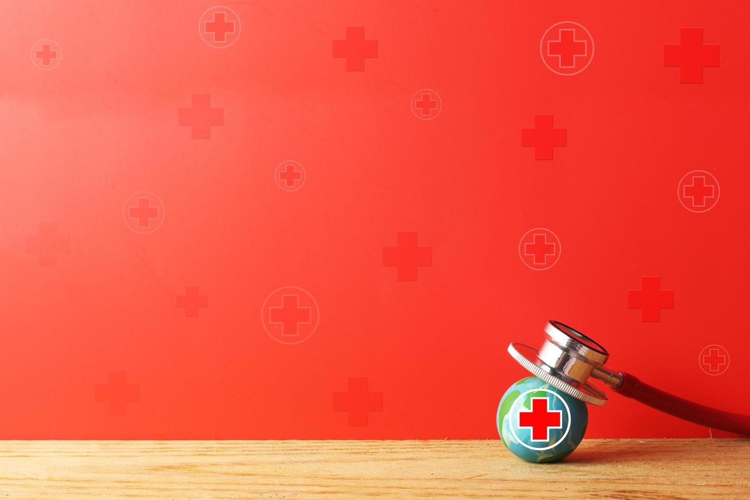 Giornata mondiale della croce rossa e della mezzaluna rossa - donatore di sangue - concetto di assistenza sanitaria internazionale - terra con croce rossa e stetoscopio su sfondo rosso foto