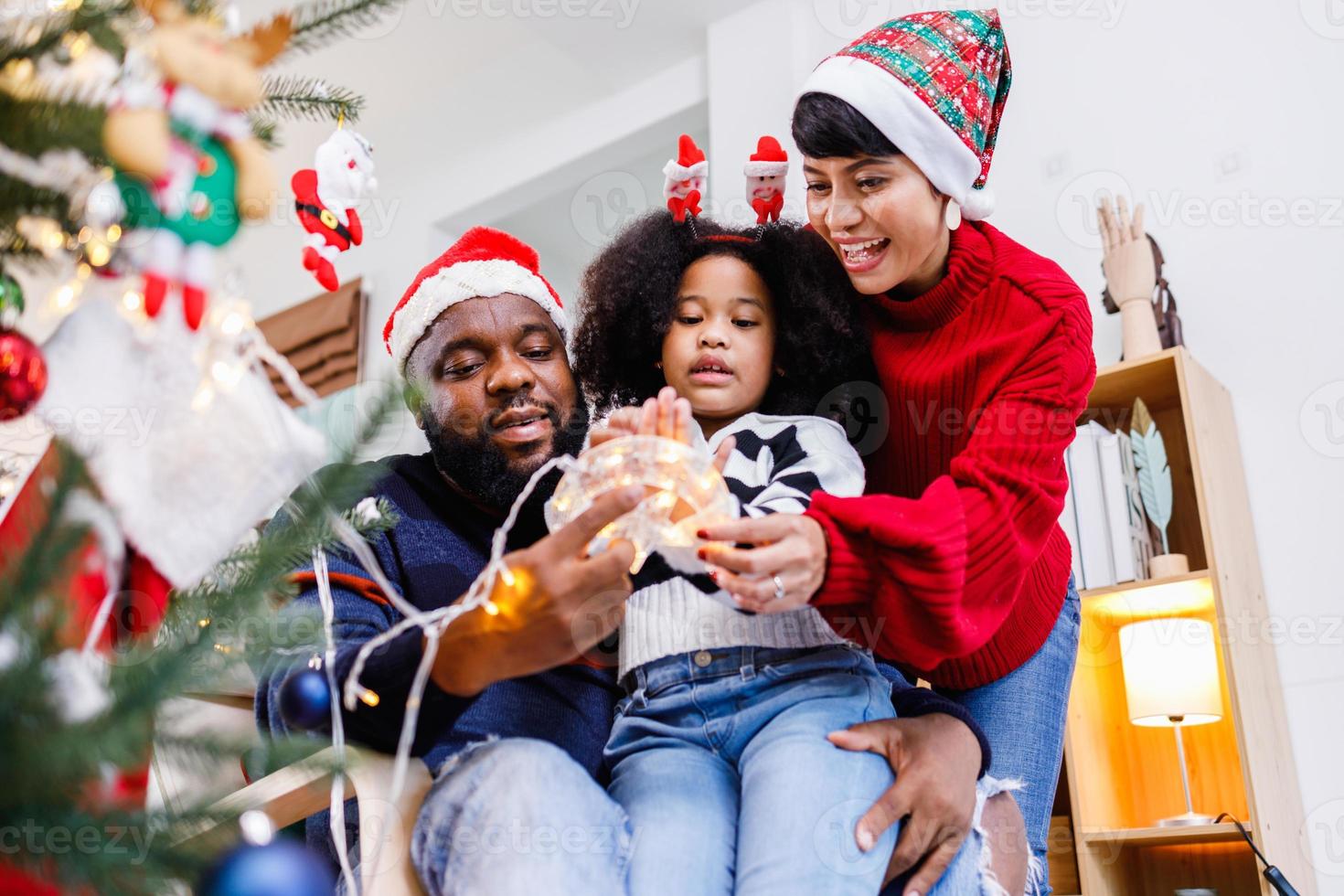 la famiglia afroamericana aiuta a decorare l'albero di natale a casa. buon Natale. foto