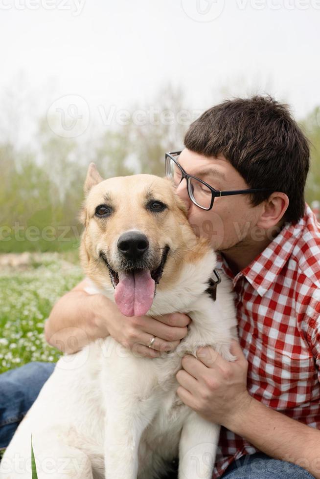 uomo felice seduto con cane pastore di razza mista su erba verde in fiori di primavera foto