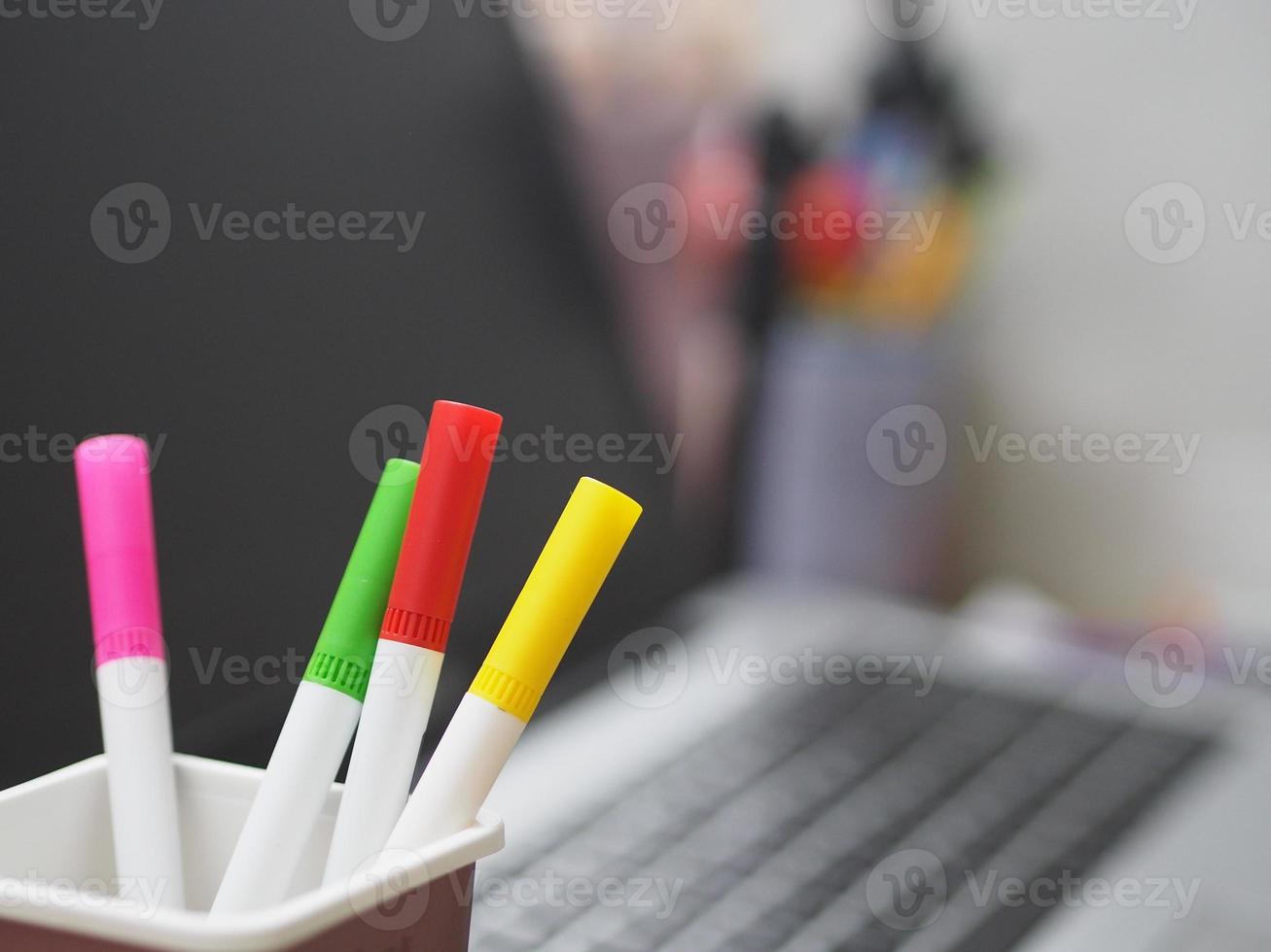 molte penne magiche di colore rosso, rosa, giallo, verde in scatola di plastica marrone, sfocate sullo sfondo del taccuino foto