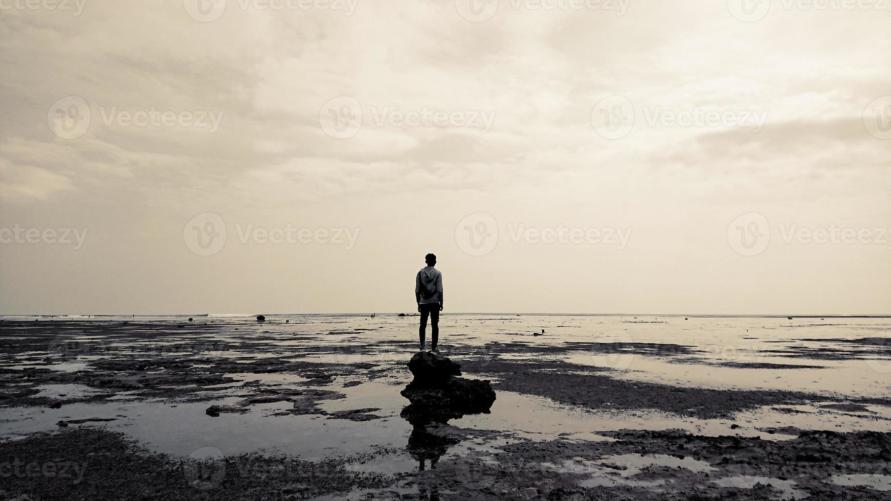 un uomo in piedi su una roccia vicino alla spiaggia foto