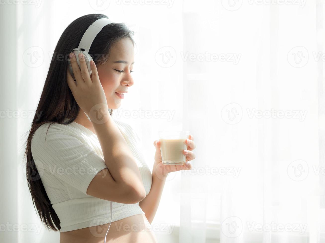belle donne incinte ascoltano musica dalle cuffie e bevono latte di soia foto