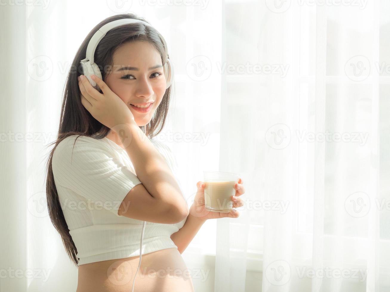belle donne incinte ascoltano musica dalle cuffie e bevono latte di soia foto