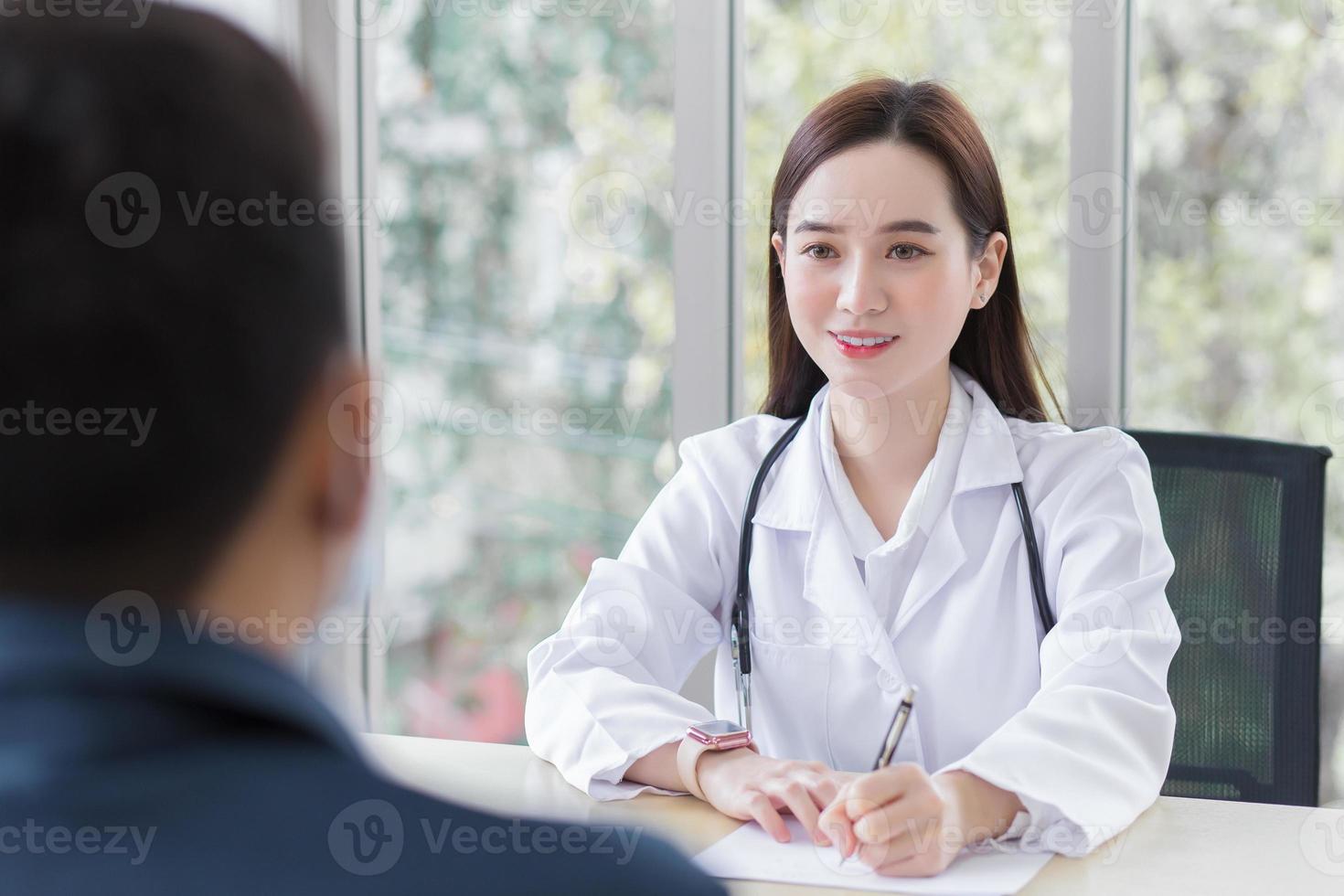 una dottoressa professionista asiatica che indossa un cappotto medico parla con un paziente uomo per consultarlo e suggerirgli informazioni sanitarie. foto