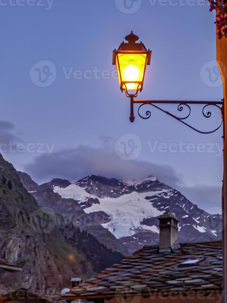 un'inquadratura verticale di una lampada vintage illuminata vicino a montagne innevate foto