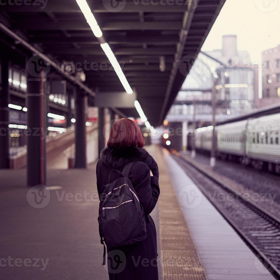 stazione ferroviaria. bella ragazza è in piedi sulla piattaforma e aspetta il treno. la donna viaggia leggera foto