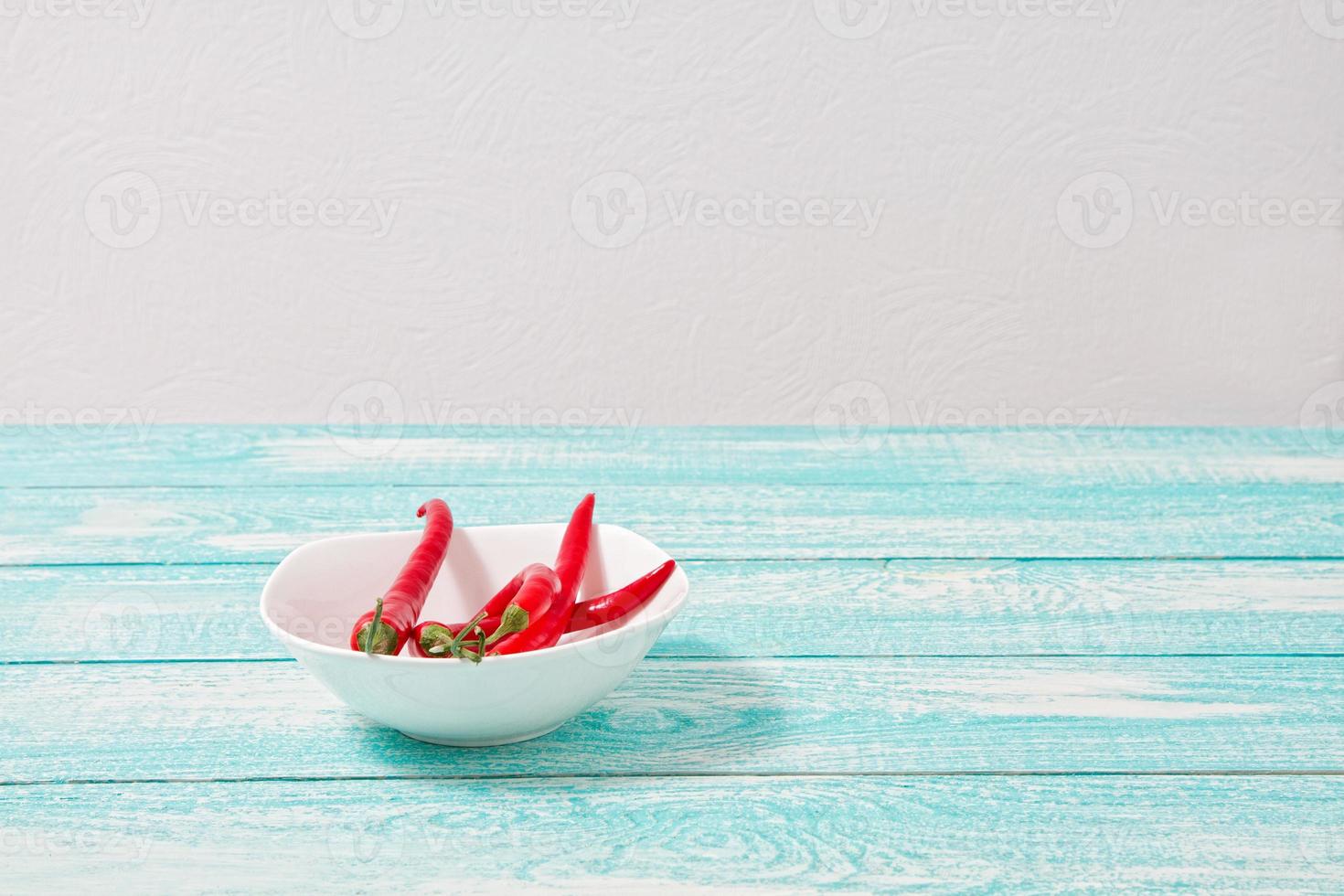 decorazione di peperoncino rosso su tavola di legno blu. impostare, copiare spazio, simulare. Caienna sul piatto bianco foto