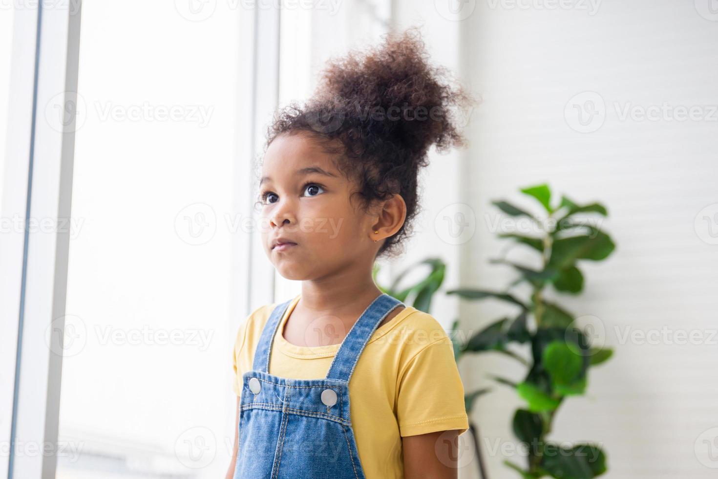 bambina che guarda fuori attraverso la finestra, bambino in piedi nel soggiorno e guardando attraverso la finestra foto