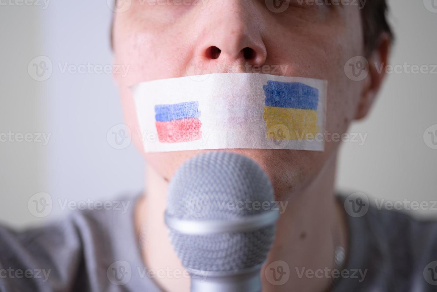 una bocca con del nastro adesivo con una bandiera della russia e dell'ucraina che cerca di parlare in un microfono. foto