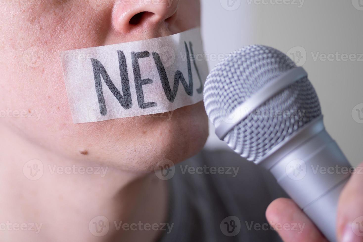 un uomo si imbavaglia la bocca con del nastro adesivo dicendo notizie cercando di parlare in un microfono. foto