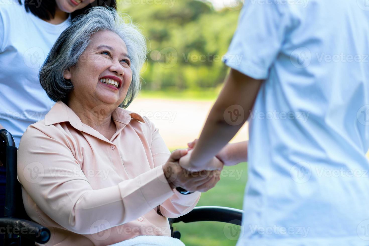 felice nonna asiatica senior in sedia a rotelle con sua figlia e nipote nel parco, nipote è venuto a visitare la nonna anziana e a tenersi per mano. concetto di famiglia felice e buon rapporto insieme foto