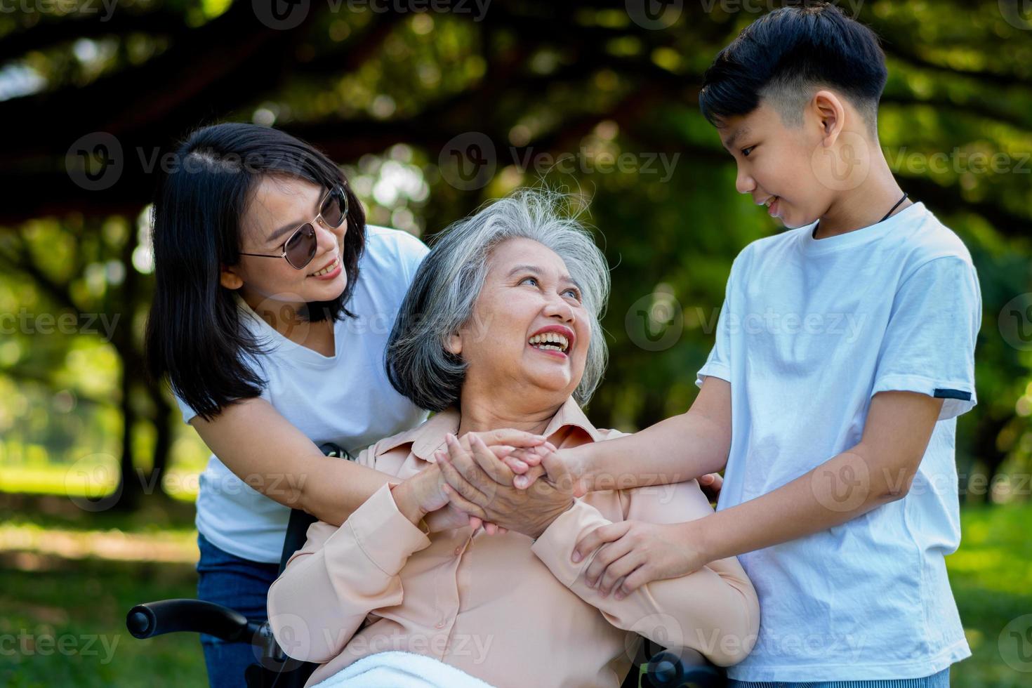 la nonna asiatica anziana felice usa la sedia a rotelle con sua figlia e suo nipote nel parco, il nipote è venuto a visitare la nonna anziana e si è tenuto per mano. concetto di famiglia felice, buon rapporto insieme foto