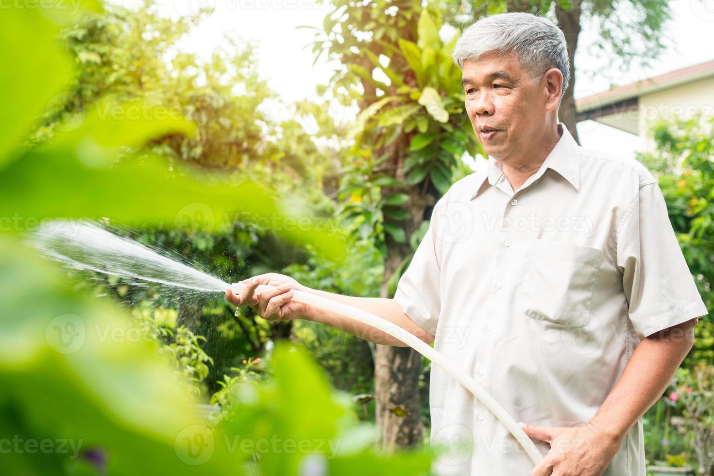 un anziano asiatico felice e sorridente sta innaffiando piante e fiori per un hobby dopo il pensionamento in una casa. concetto di uno stile di vita felice e di una buona salute per gli anziani. foto