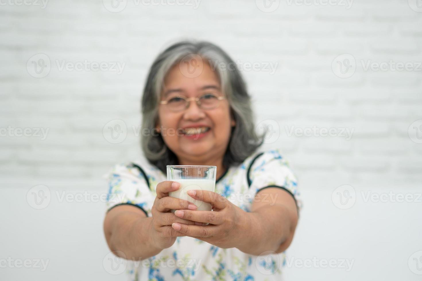 donna anziana asiatica che tiene il latte di vetro mentre ci si rilassa su un divano soggiorno per il benessere in pensione. donna anziana che beve un bicchiere di latte per mantenere il suo benessere. concetto di benessere e salute. foto
