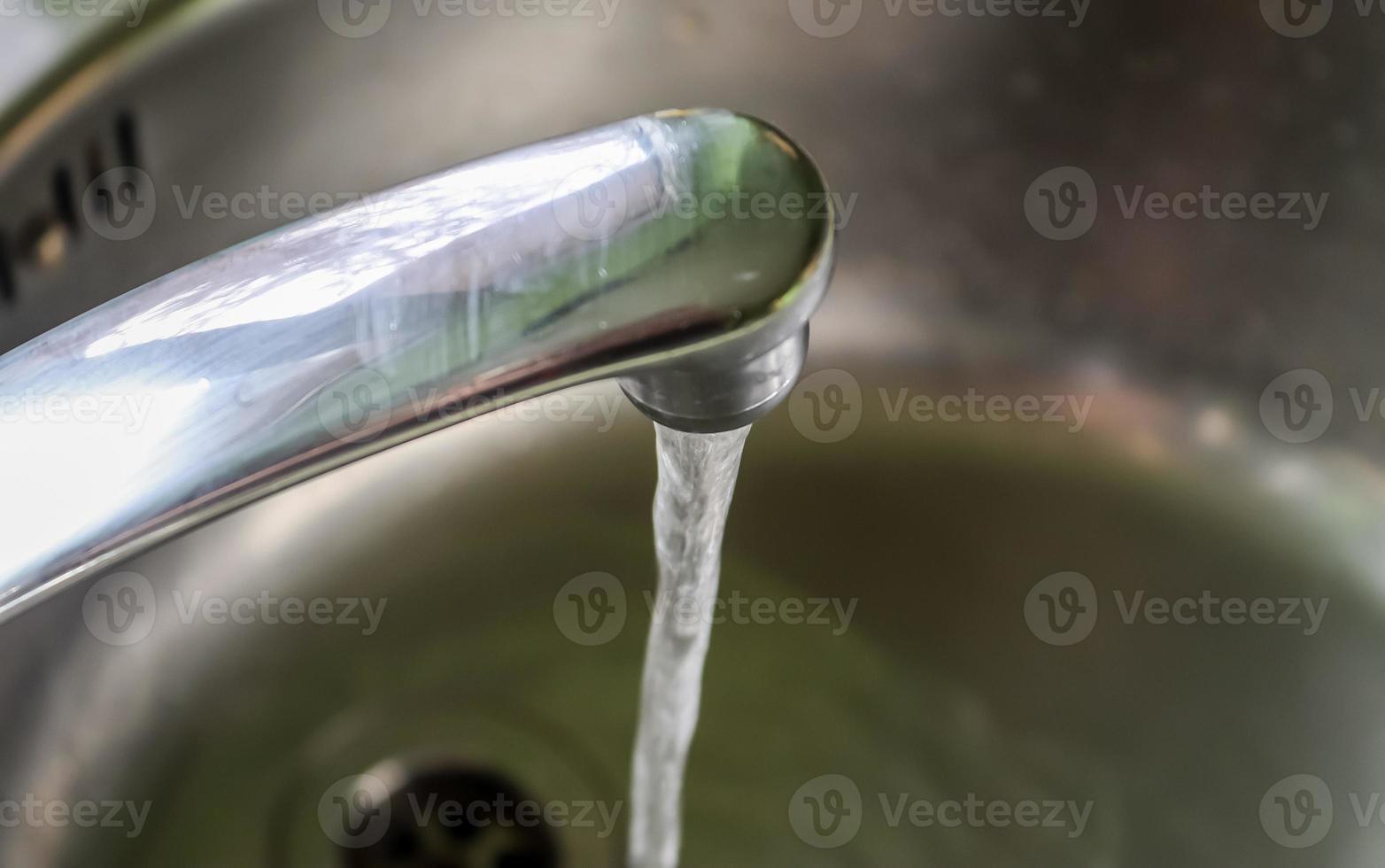 acqua corrente da un rubinetto nello scarico di un lavandino cromato. foto