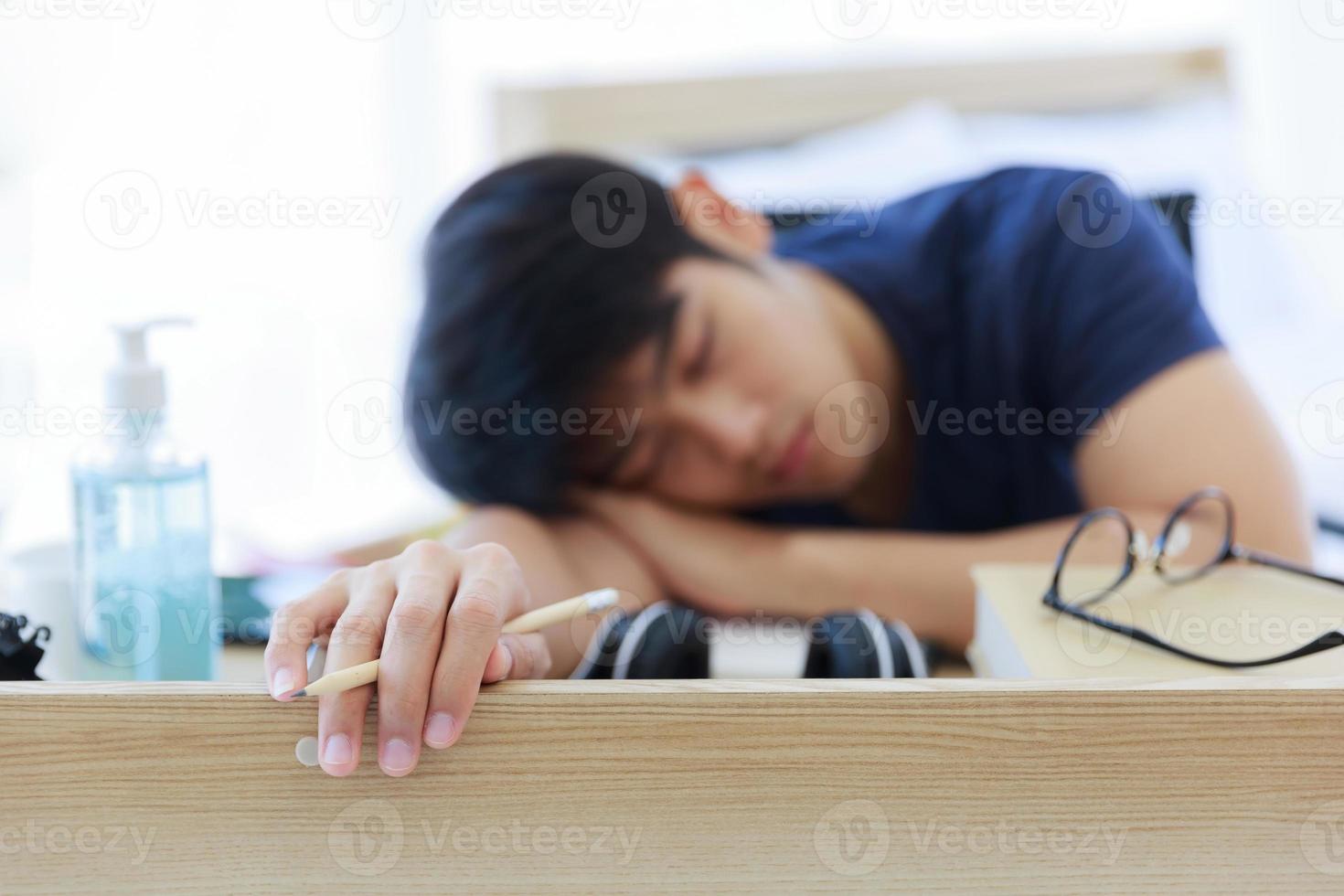 un uomo asiatico seduto e dormire alla scrivania con una matita in mano in camera da letto. foto