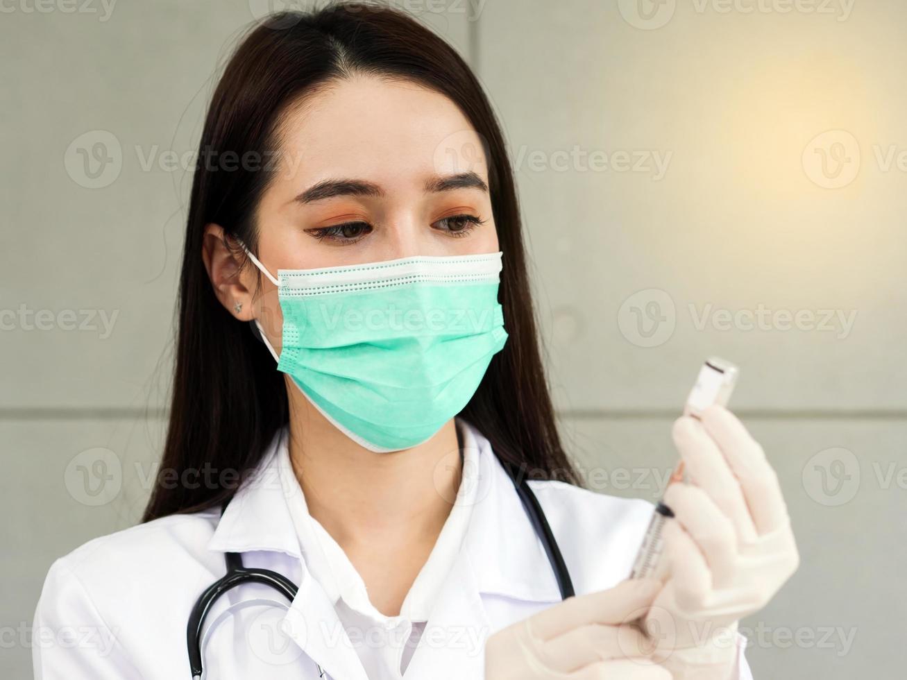 una dottoressa o un'infermiera con una maschera chirurgica sta preparando una siringa e un vaccino. preparazione medica per la vaccinazione dei pazienti, primo piano sul viso di un medico. foto