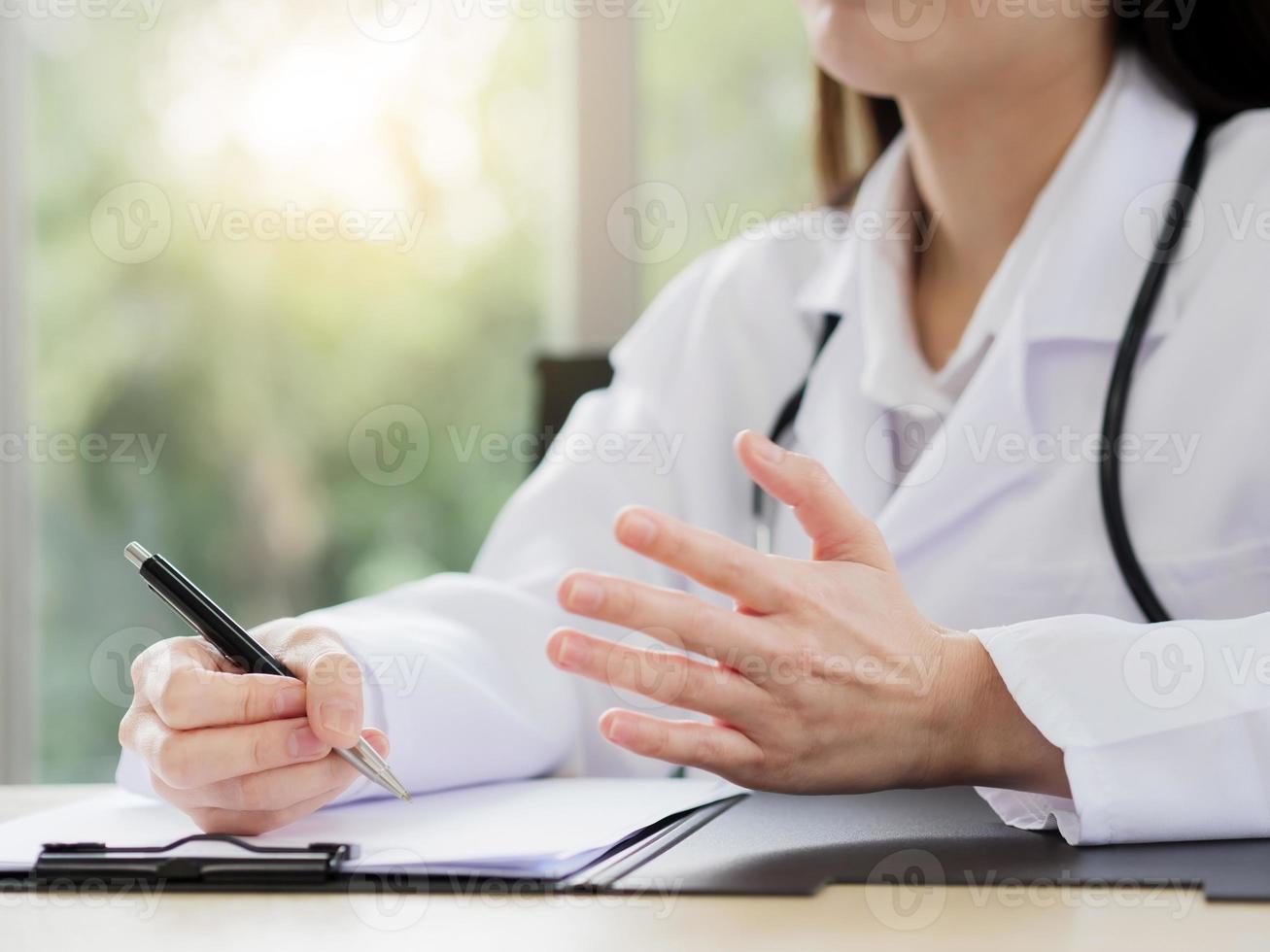 un primo piano della mano di una dottoressa o di un'infermiera tiene in mano una penna e usa un'altra mano per spiegare informazioni o qualcosa con uno sfondo sfocato. foto