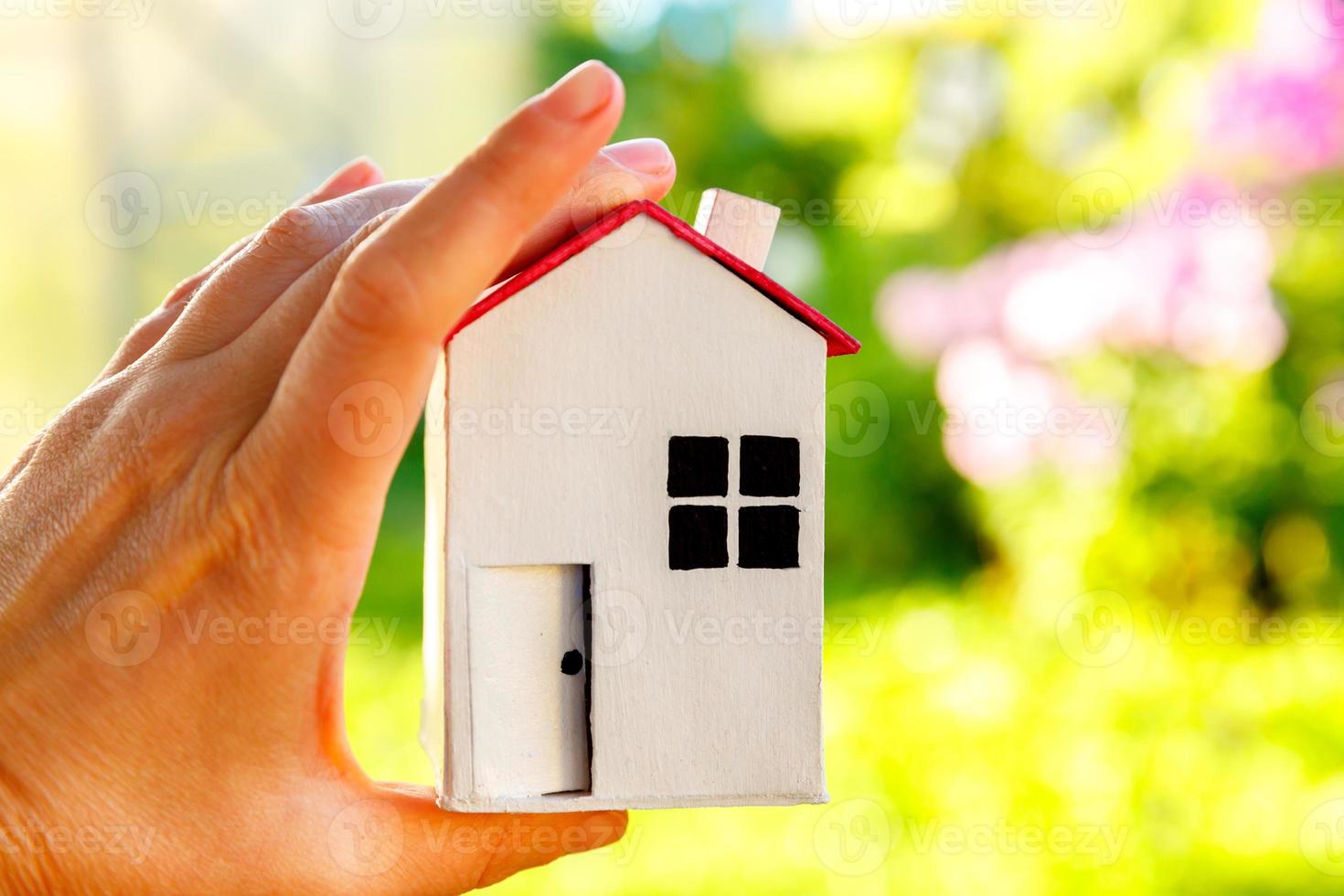 casa modello in miniatura in mano di donna femminile su sfondo verde all'aperto. villaggio ecologico, sfondo ambientale astratto. concetto di ecologia della casa dei sogni di assicurazione sulla proprietà dei mutui immobiliari. foto