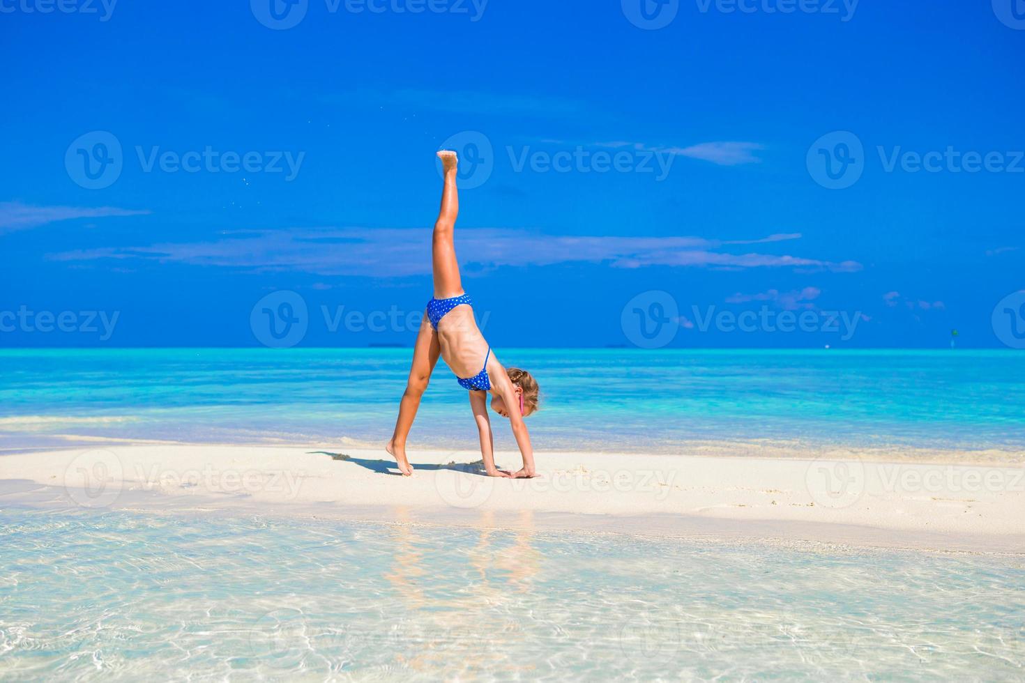 adorabile bambina che si diverte a fare la ruota di carro sulla spiaggia di sabbia bianca tropicale foto