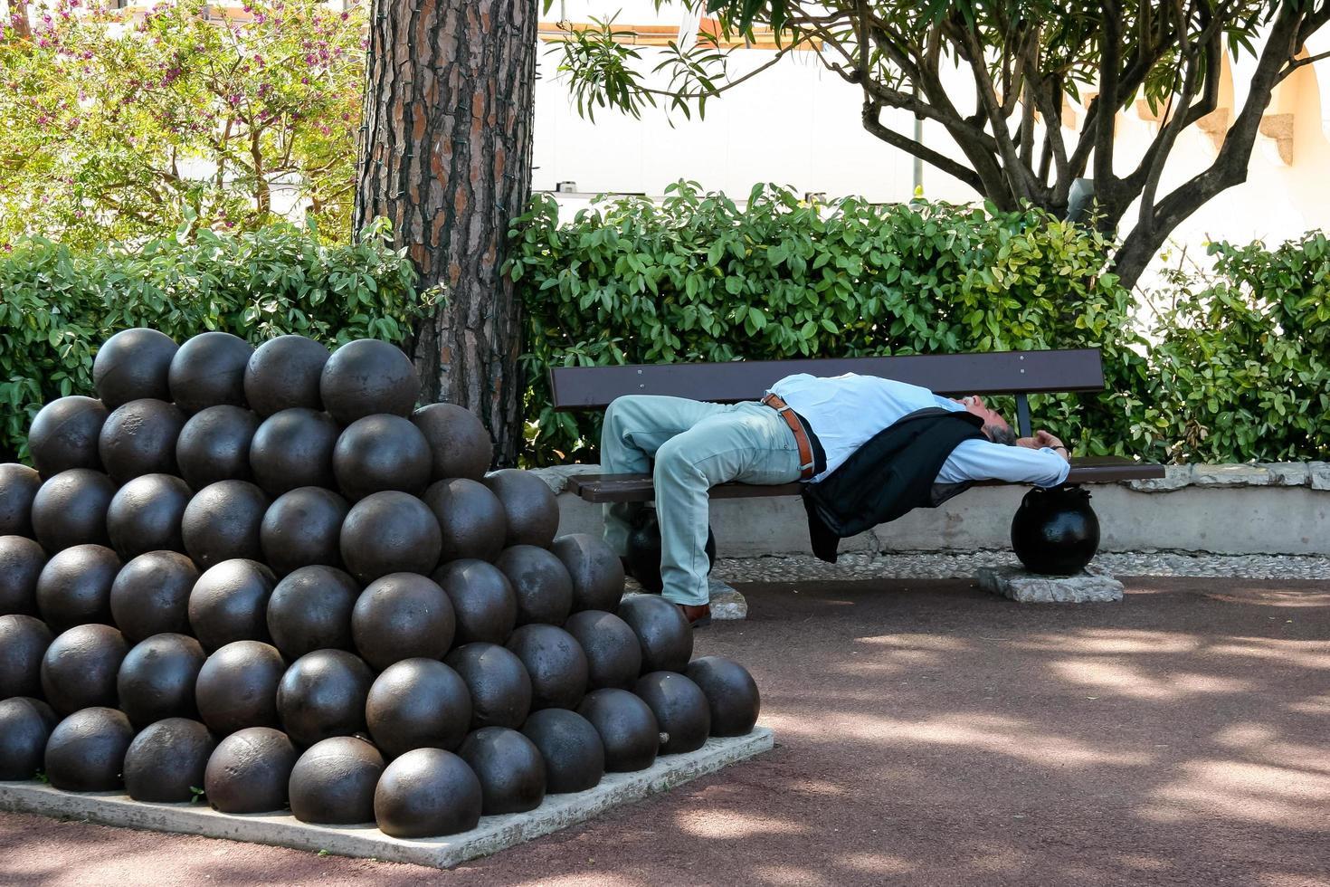 monte carlo, monaco, 2006. uomo addormentato all'ombra accanto a un mucchio di palle canoniche foto