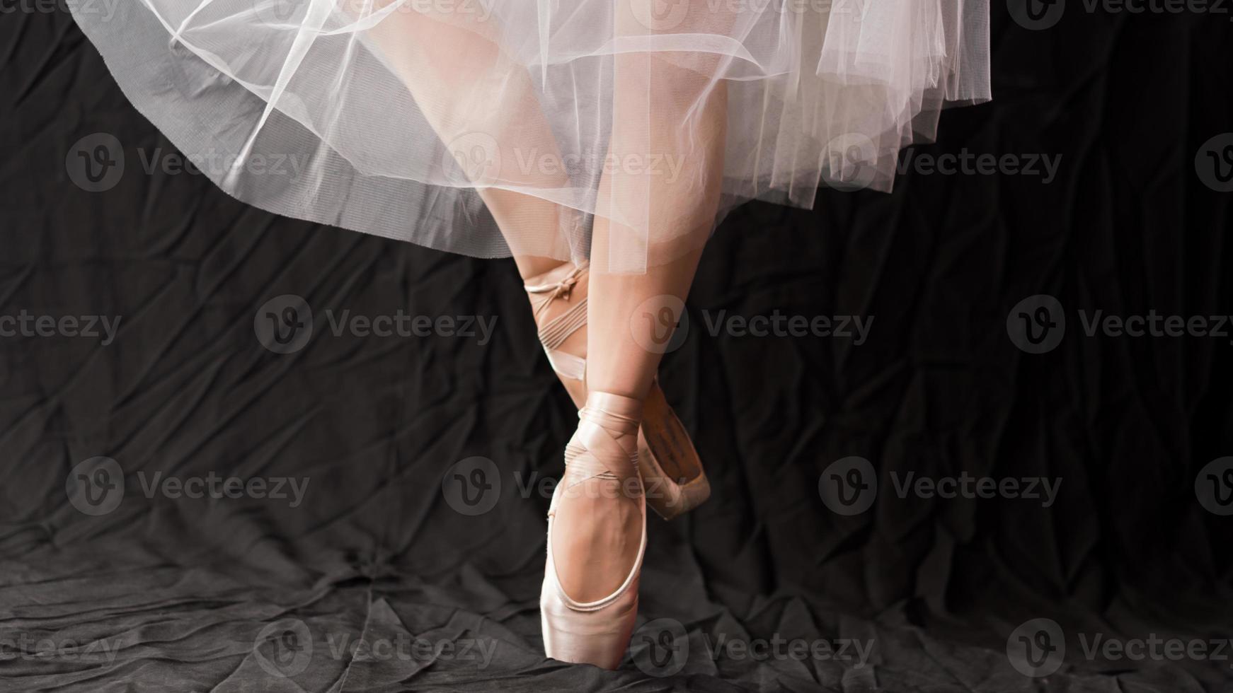 primo piano delle gambe danzanti della ballerina che indossa una punta bianca su sfondo nero. foto